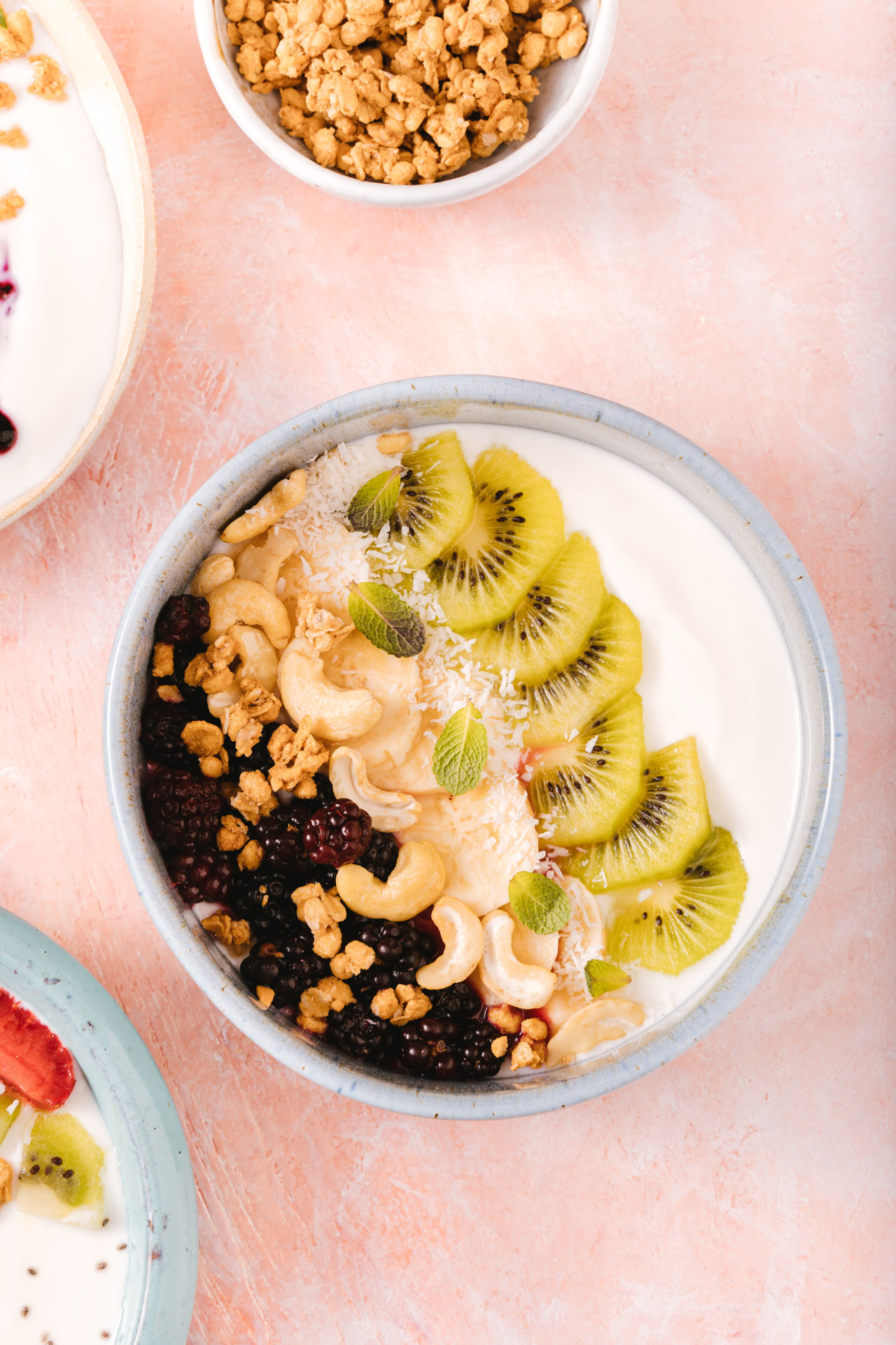 Verse yoghurtbowl met kiwi, bramen, cashewnoten, granola en munt op een roze ondergrond
