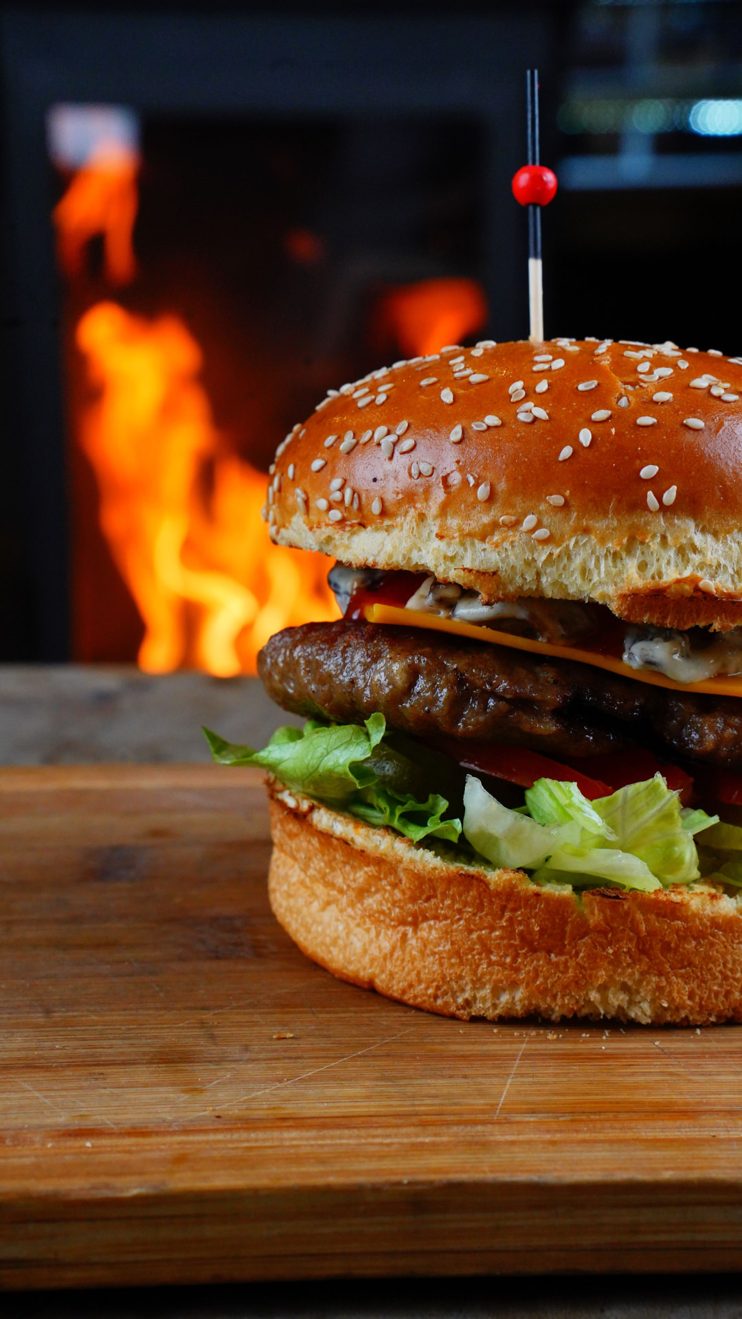 Huisgemaakte sesamburger met gesmolten kaas, sla en tomaat op een houten plank, met een warme vlam op de achtergrond